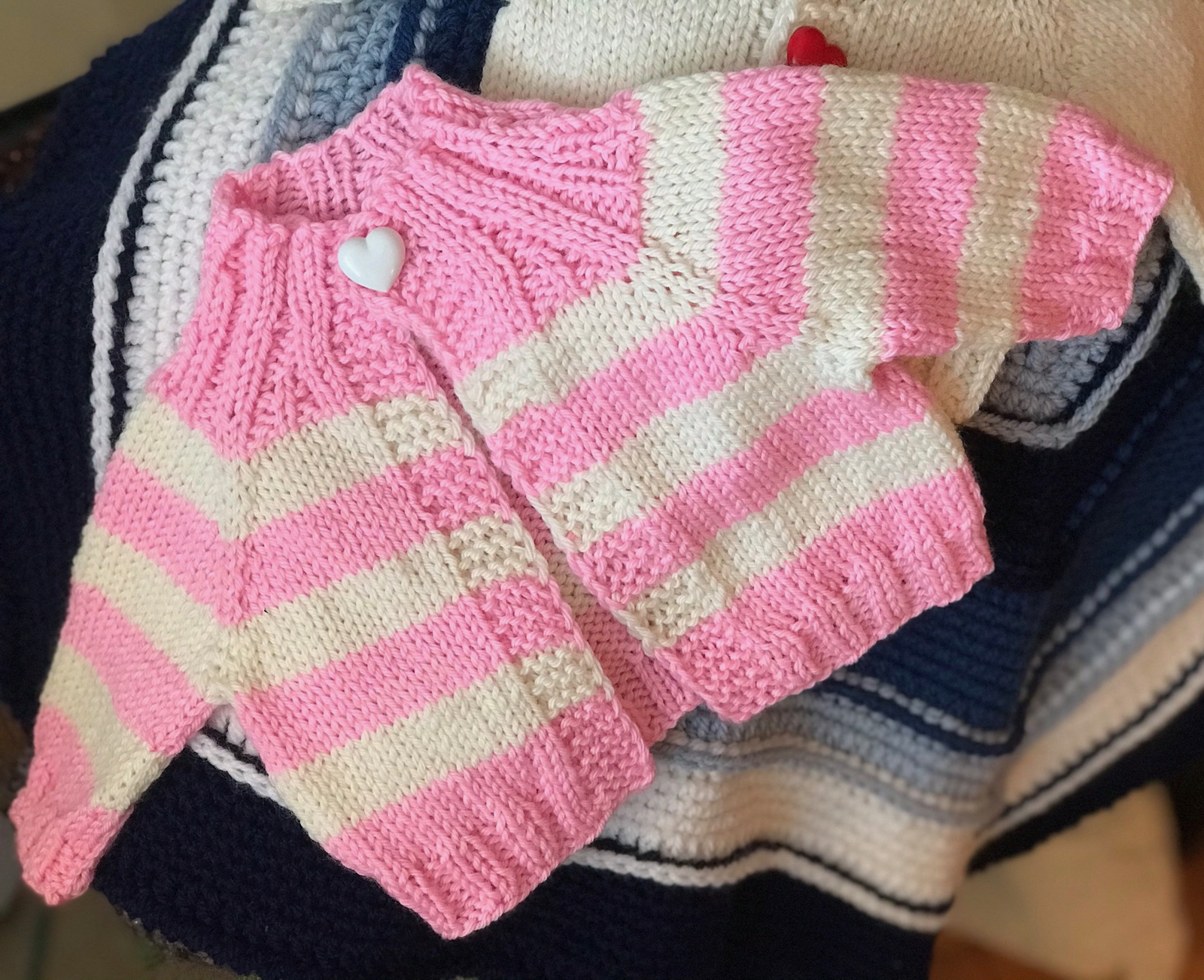 Striped Love Baby Sweater — a knitted pink and cream striped baby cardigan with a heart button